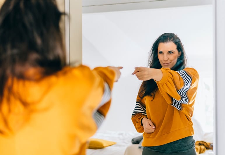 Woman pointing at her reflection in the mirror in a motivating way to show that she accepts herself.