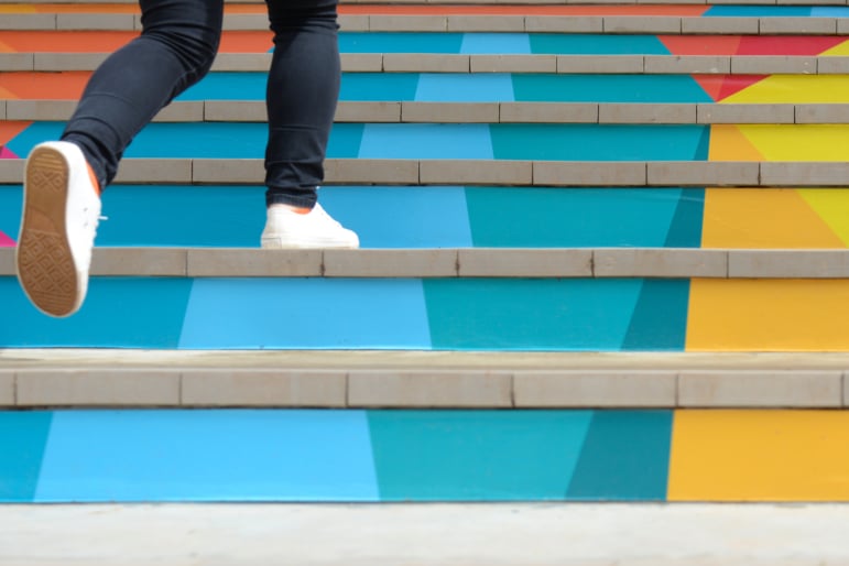 Cropped shot of legs in black pants with white tennis shoes walking up colorful steps.