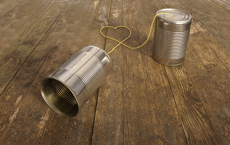 Two tin cans connected by a yellow string that forms the shape of a heart representing couples communication.