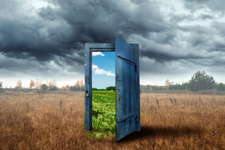 A door in a dead field on a cloudy day opened to show a green field on a sunny day
