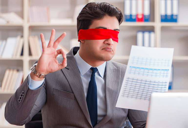 A man with a red blindfold on looking at a document while making the ok symbol with his right hand