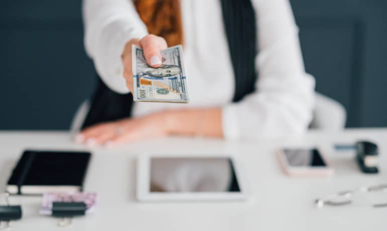 Woman sitting at desk holding out money