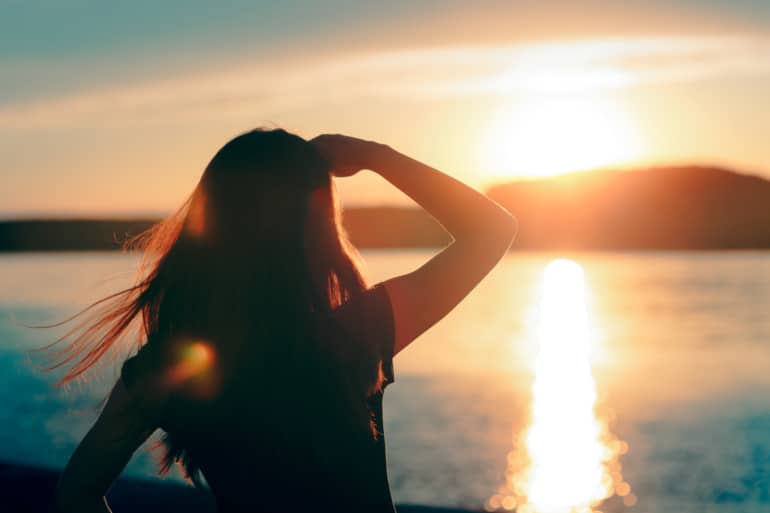 Silhouette of a woman with her hand shading her eyes from the setting sun over the water