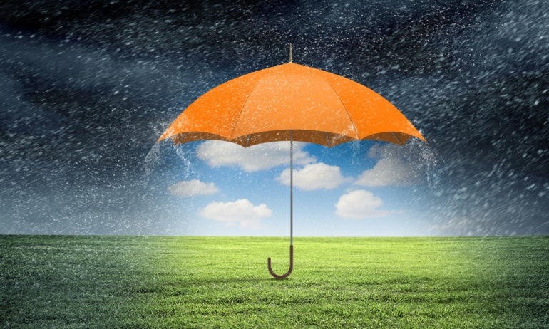 An orange umbrella holding back the dark rain sky with a sunny sky underneath