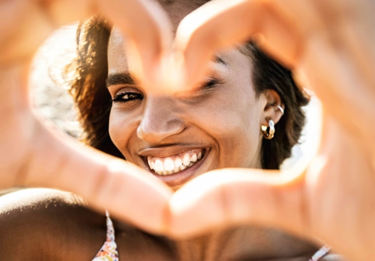 Woman smiling through her hands making the shape of a heart