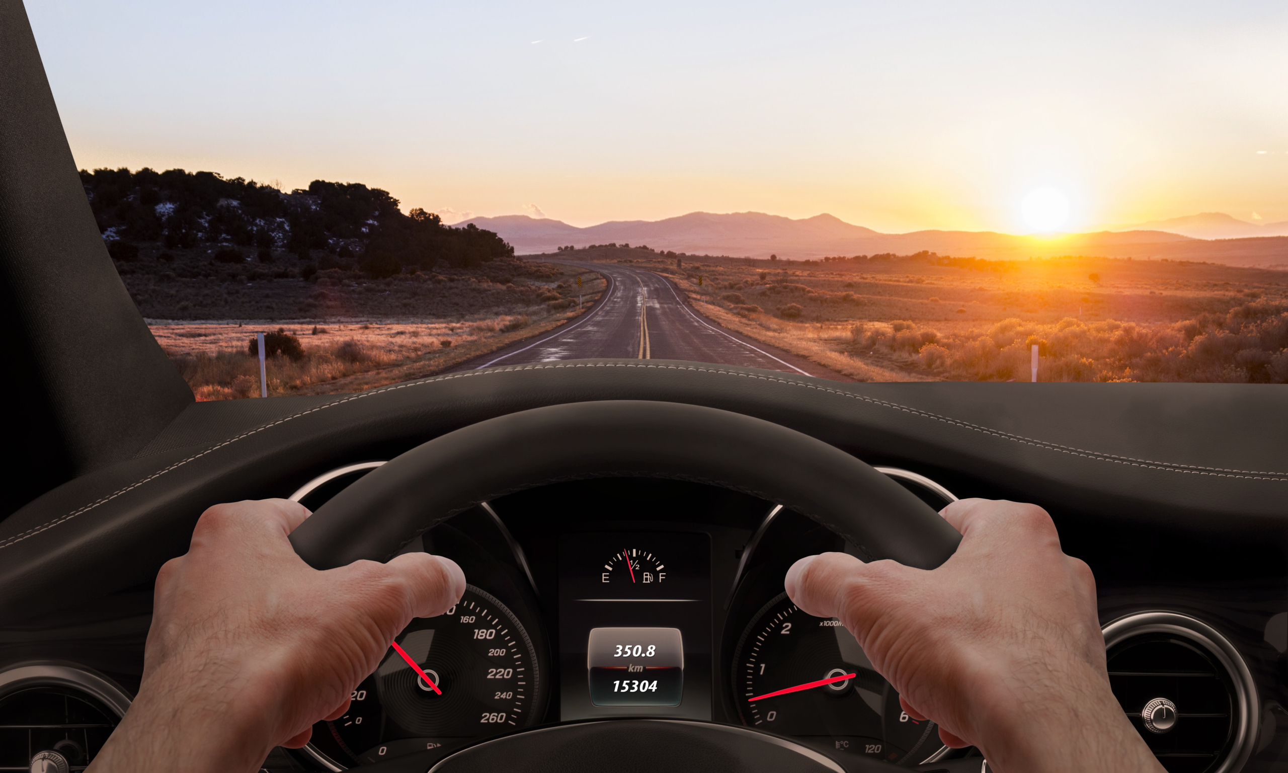 View of the sunset on the road from the driver angle while hands on the wheel.