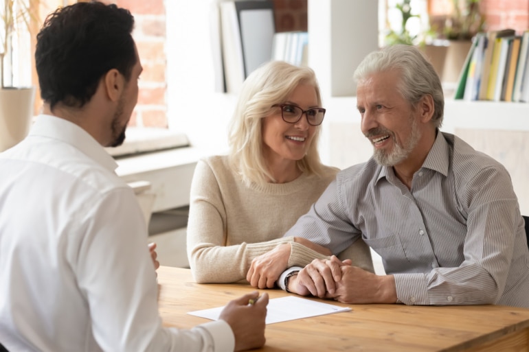 A smiling couple sitting at a desk across from a business man.