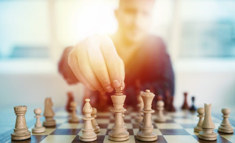 Man holding top of king chess piece on a chess board.