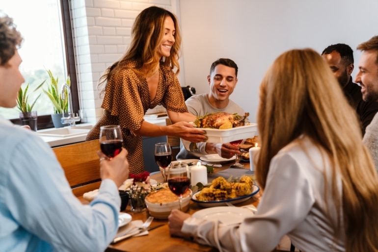 Smiling woman placing a turkey on a table for Thanksgiving dinner with friends