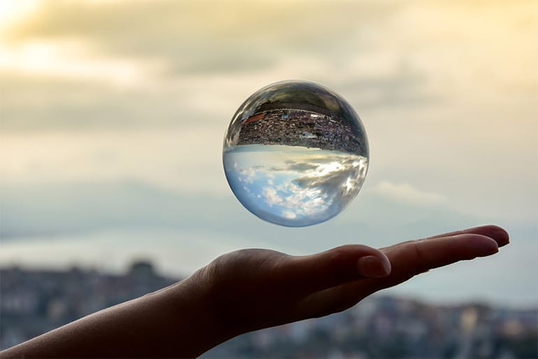Clear glass sphere with a landscape reflection floating over an outstretched palm
