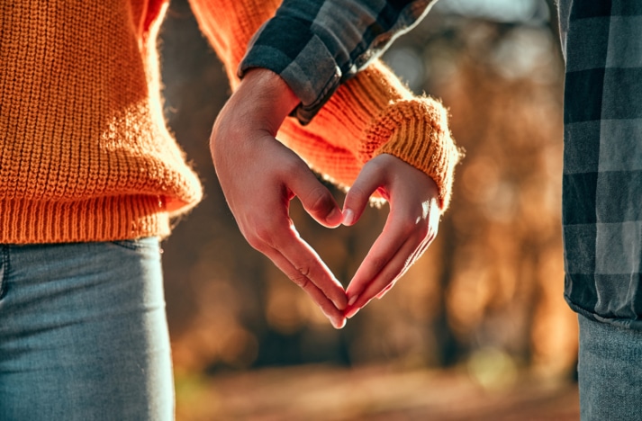 couple walking in park in autumn time focused on their hands forming the shape of a heart.