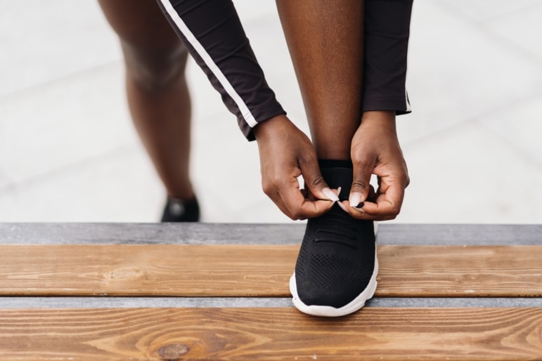 Woman with her left foot on a wooden bench tying her black sneaker.