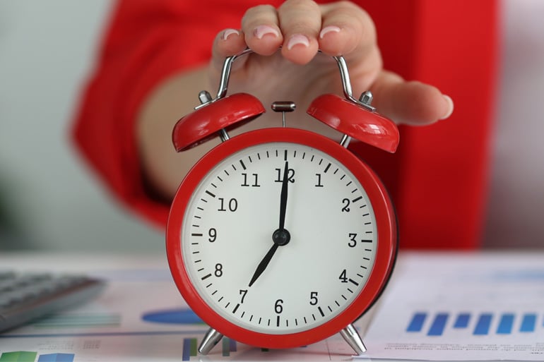 Woman in red jacket turning off red alarm clock at desk.