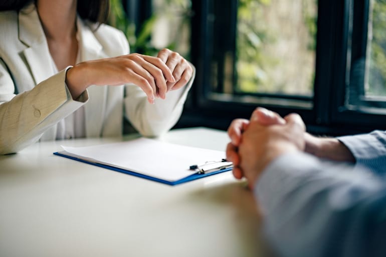 A man and a woman sitting across from a table with a close up on their hands.