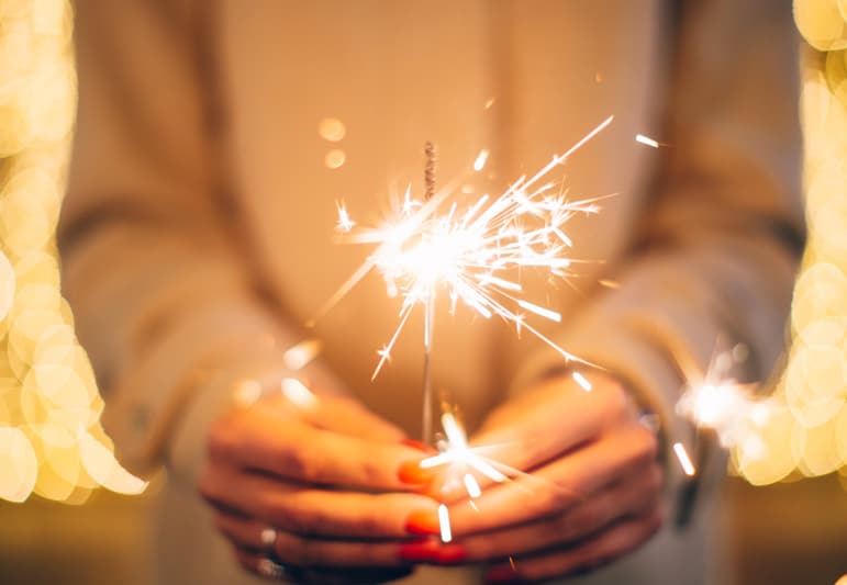 A woman holding a sparkler in front of her. Golden lighting.
