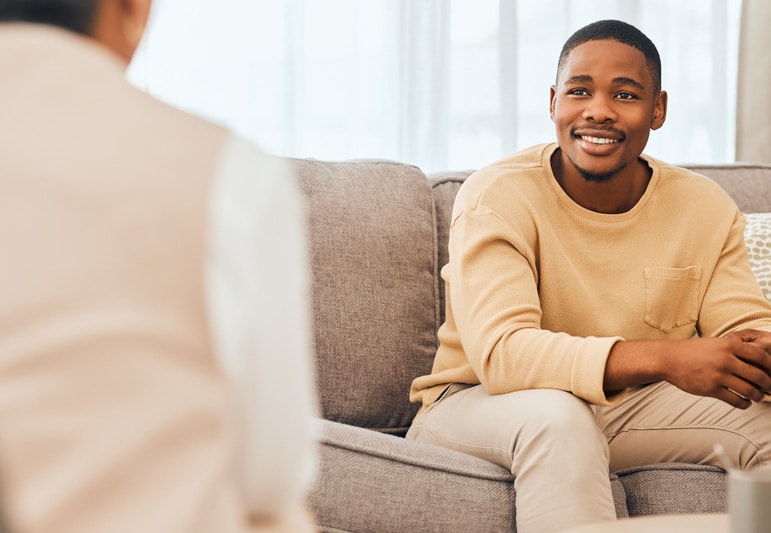 Young African american male sitting on a couch and smiling at a clinician as they discuss treatment plans.