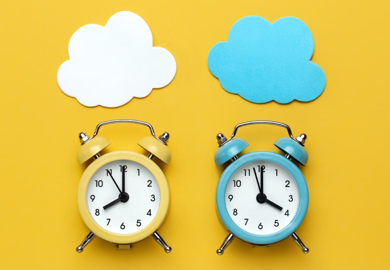 Two clocks on a yellow background. One yellow with a white cloud above it and the other blue with a blue cloud above it to signify leisure time versus wasted time.