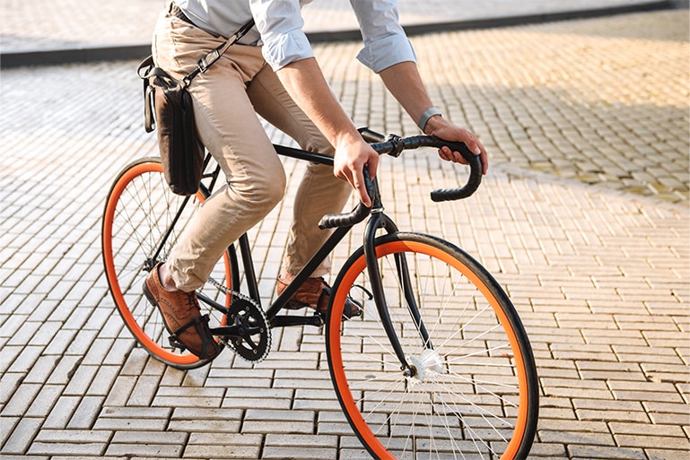 Cropped image of young stylish man dressed in shirt riding on a bicycle on a city street.