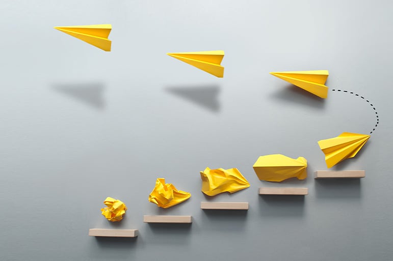 Wooden steps with different stages of making a yellow paper airplane, before taking flight, creating something from nothing