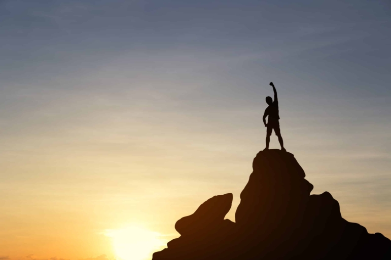 Silhouette of a young man and arm up on top mountain at sunset. Business, achievement, success, concept.