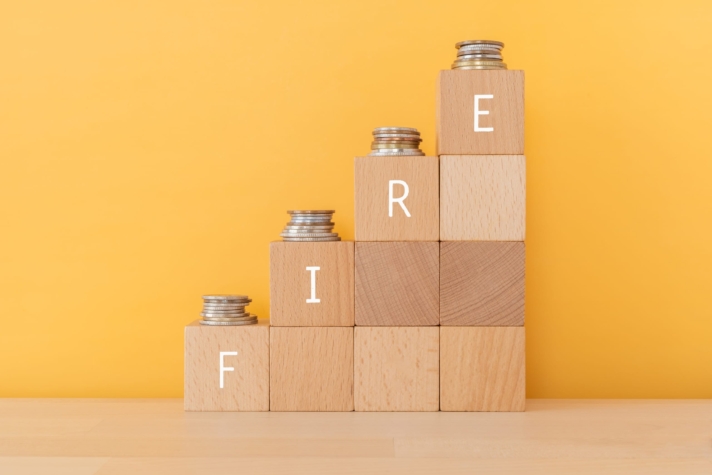 Rising stacked wooden blocks topped with coins with FIRE spelled out representing Financial Independence Retire Early.