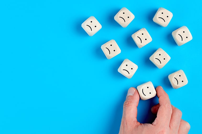 Male hand chooses the happy face among unhappy faces on wooden blocks. Concept of customer satisfaction or positive feedback.