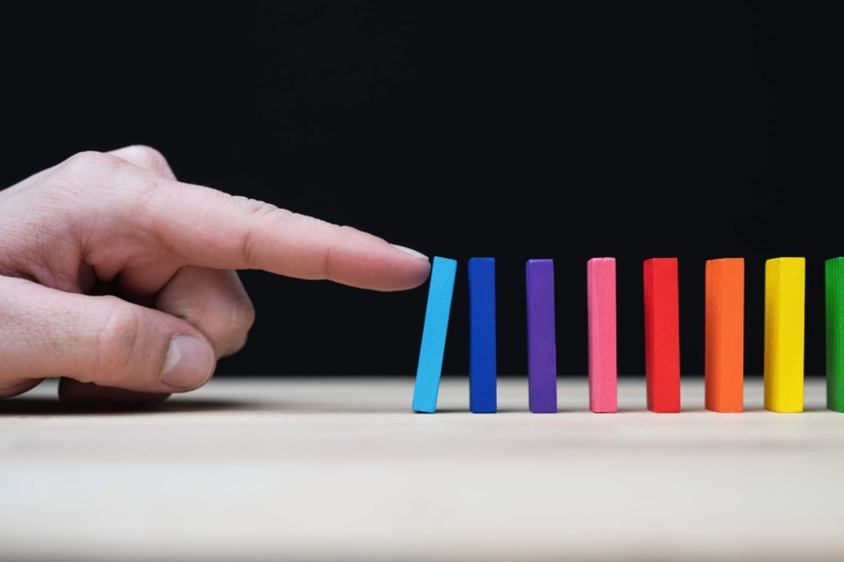 a hand starting a chain reaction with colored dominoes.