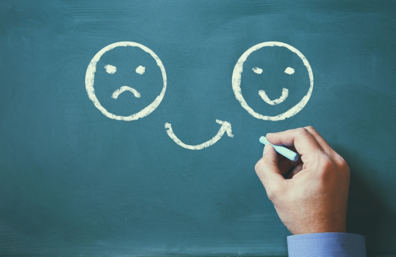 hand drawing an unhappy smiley face that changes to a happy smiley faces on a chalkboard.