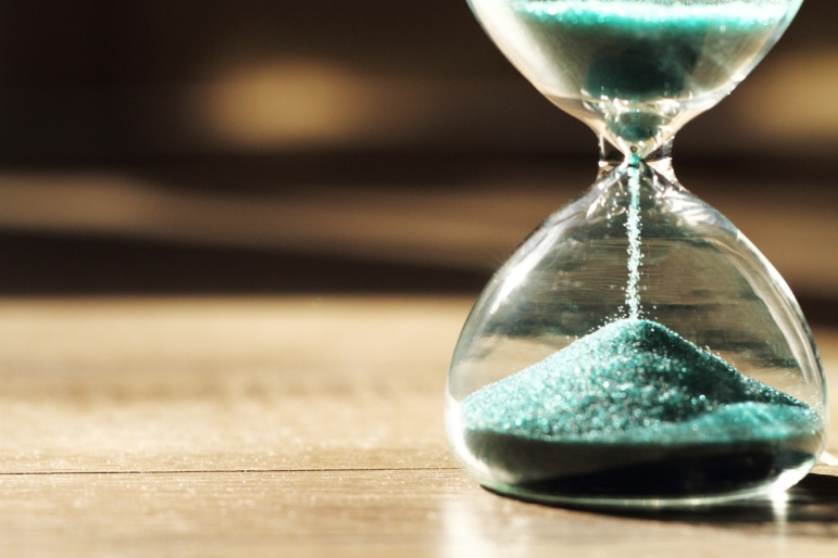 Sand running through the bulbs of an hourglass measuring the passing time in a countdown to a deadline, on a dark background