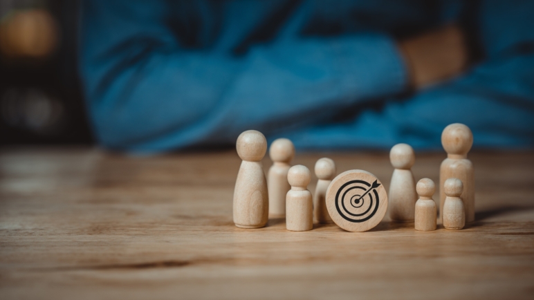 A group of small wooden figures surrounding a wooden archery target symbolizing the relationship of your goals to your surroundings.