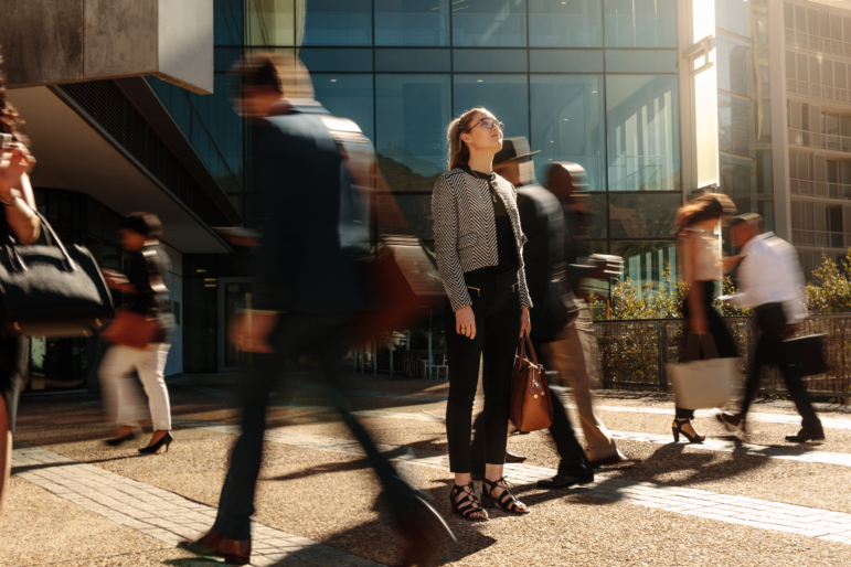 Woman standing still and calm while blurred crowds rush past her on a city street, symbolizing the unnoticed burden of chronic stress in a fast-paced world.