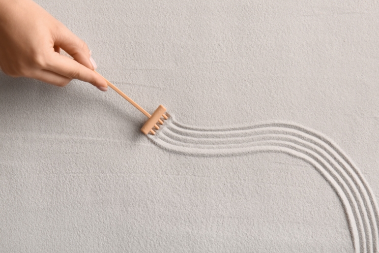 A hand carefully rakes smooth, curving lines through fine sand, creating gentle order and flow. A quiet metaphor for finding balance and alignment in the midst of life’s natural shifts.