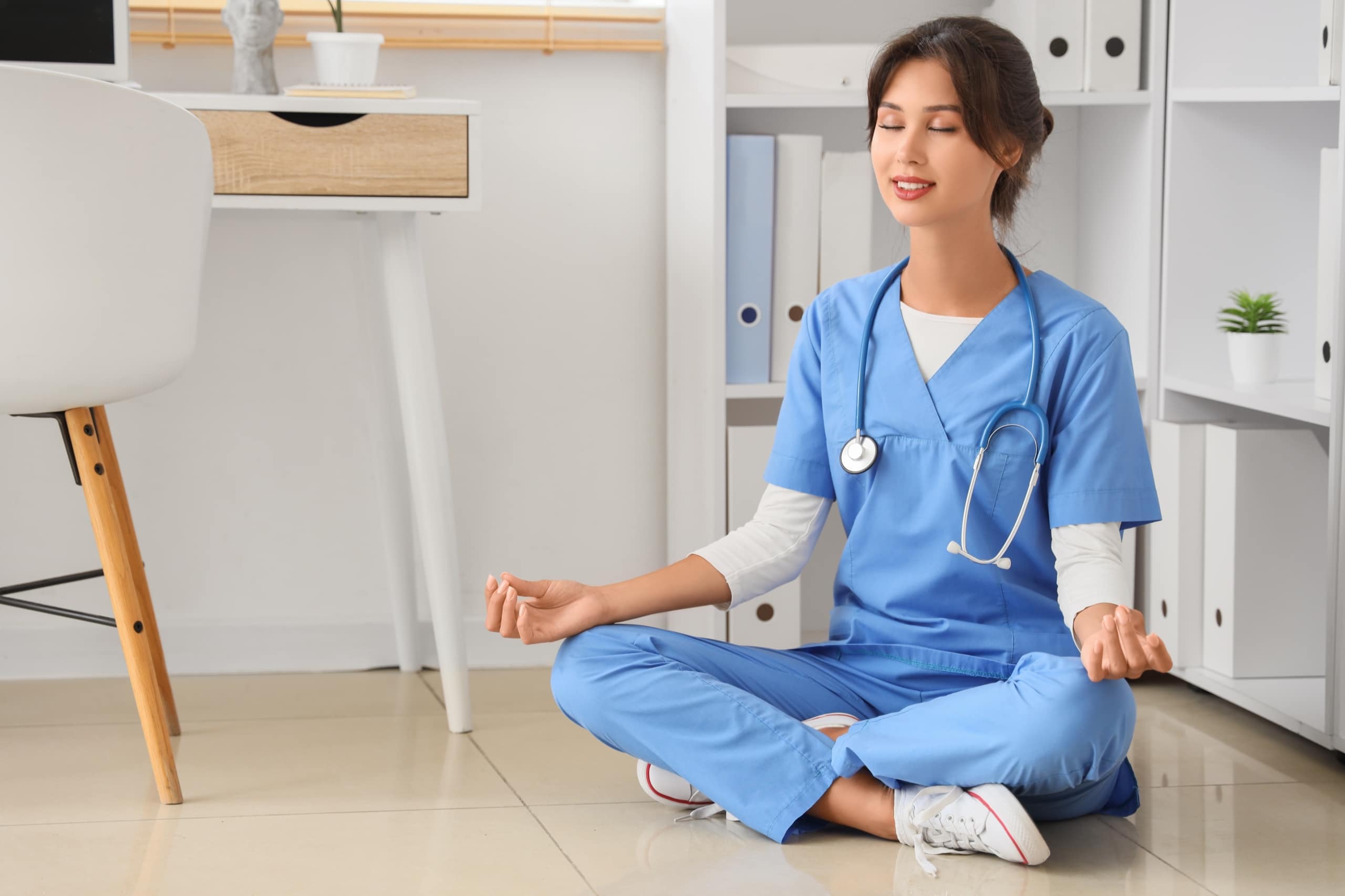 Physician in scrubs practicing mindfulness meditation during a break, representing intentional stress management and well-being in medical practice.
